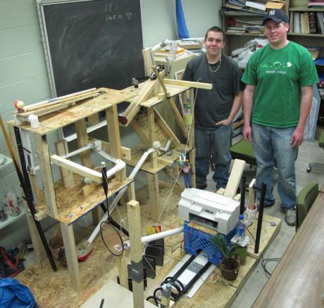 •	GCC engineering students David Simmons (left) and Matt Klotzback (right) standing with their plant watering, award winning Rube Goldberg Machine 